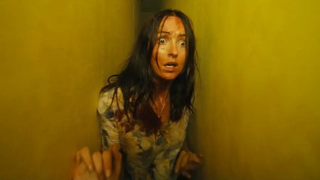 A disheveled Mary Kline looking scared while being stuck between two yellow walls in A24's Backrooms movie