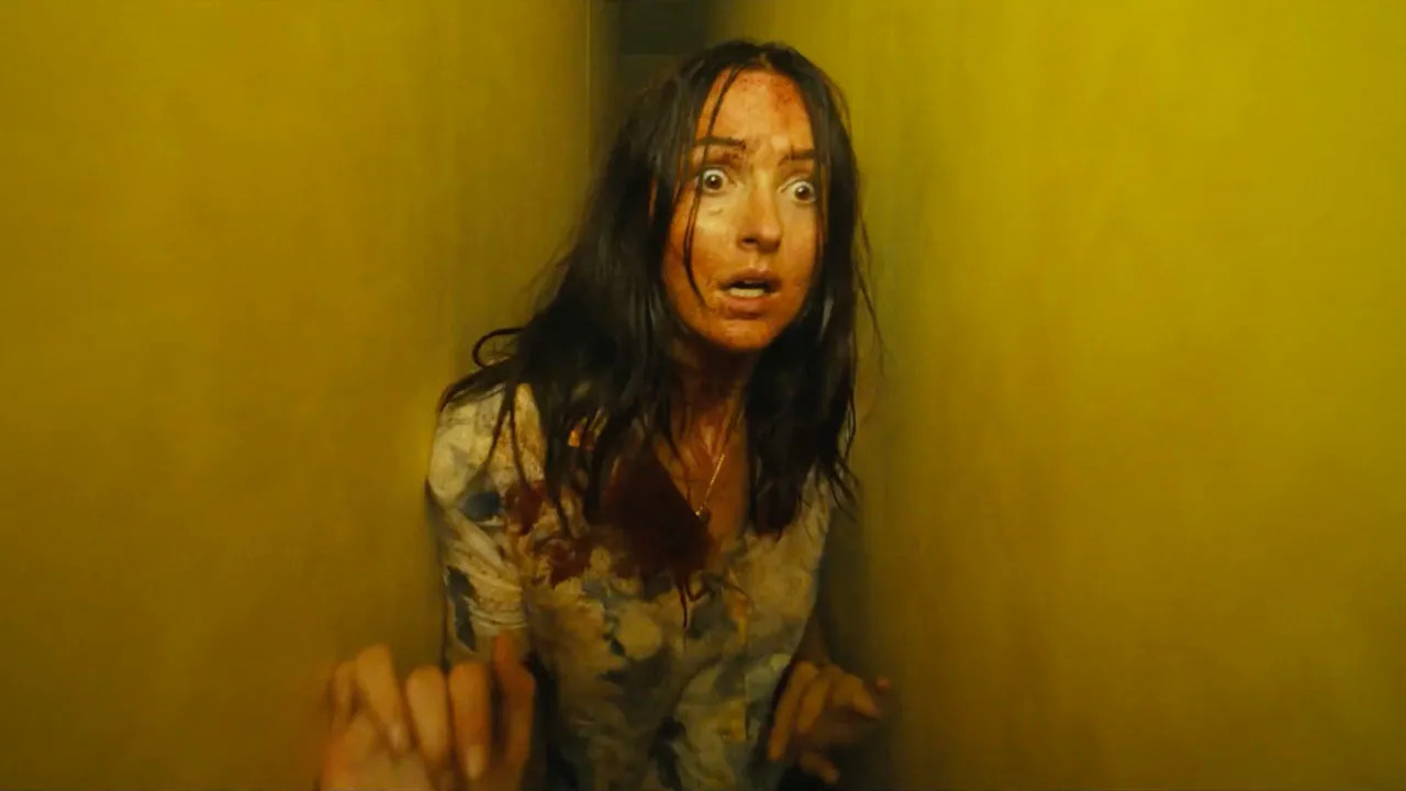 A disheveled Mary Kline looking scared while being stuck between two yellow walls in A24's Backrooms movie