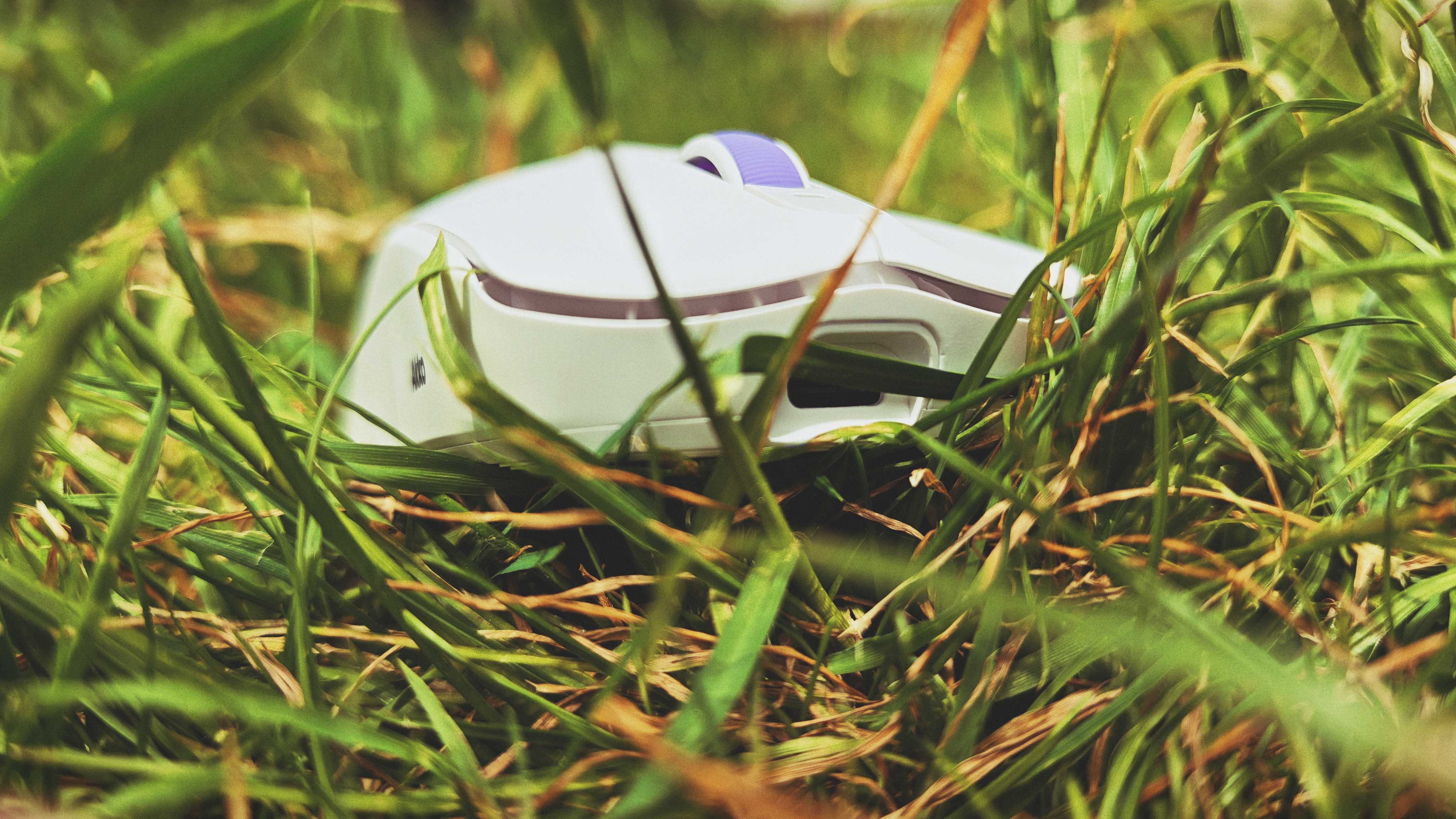 A white and purple Akko Dash Ultra gaming mouse sitting in tall grass in a garden