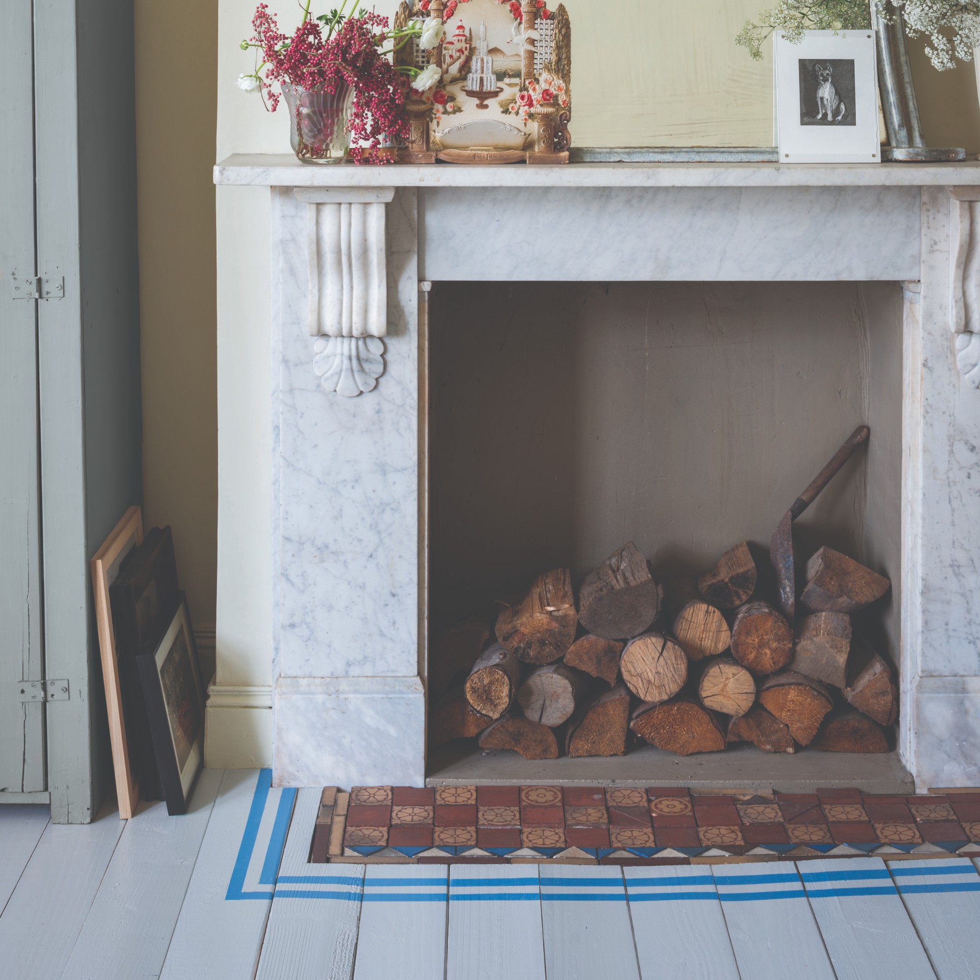 A marble fireplace highlighted by a blue border painted on wooden floor otherwise painted in grey