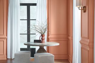 A living room with a marble table and checked stools and walls painted a terracotta color