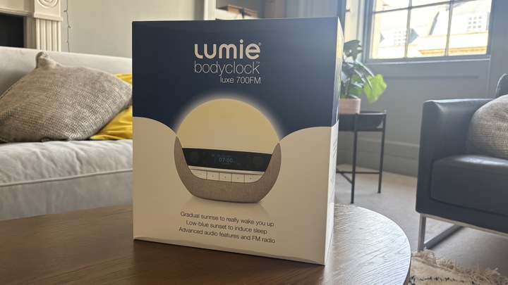 The Lumie Bodyclock Luxe 700FM sunrise alarm in its box and placed on a coffee table. 