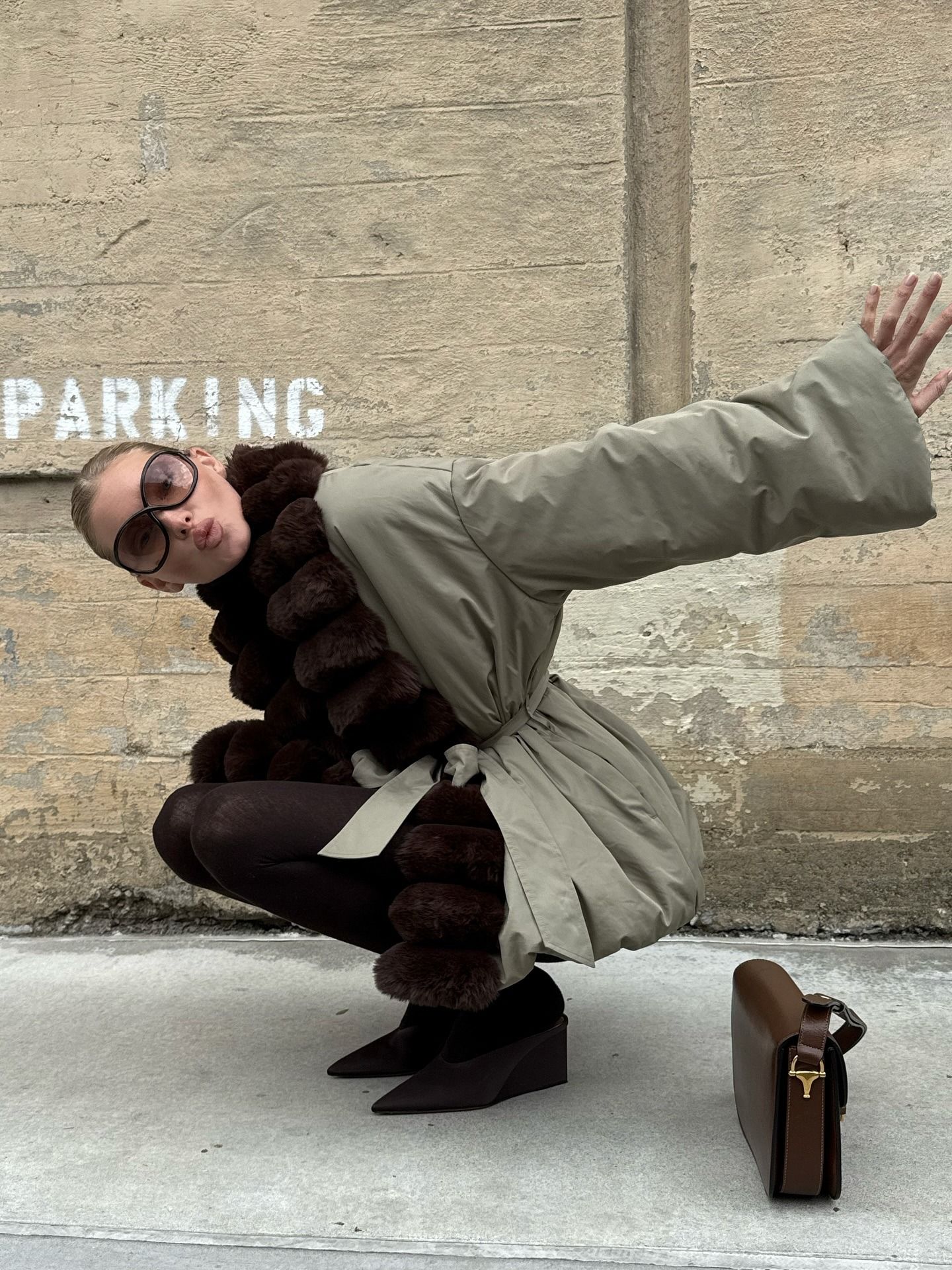 Elsa Hosk wearing a fur-trimmed parka, brown tights, and brown Alaia satin mules