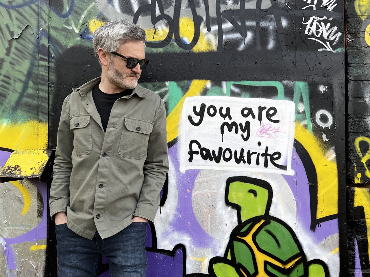 A man standing in front of a wall of graffiti