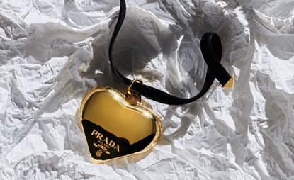 Prada gold heart on black necklace, resting on crumpled paper