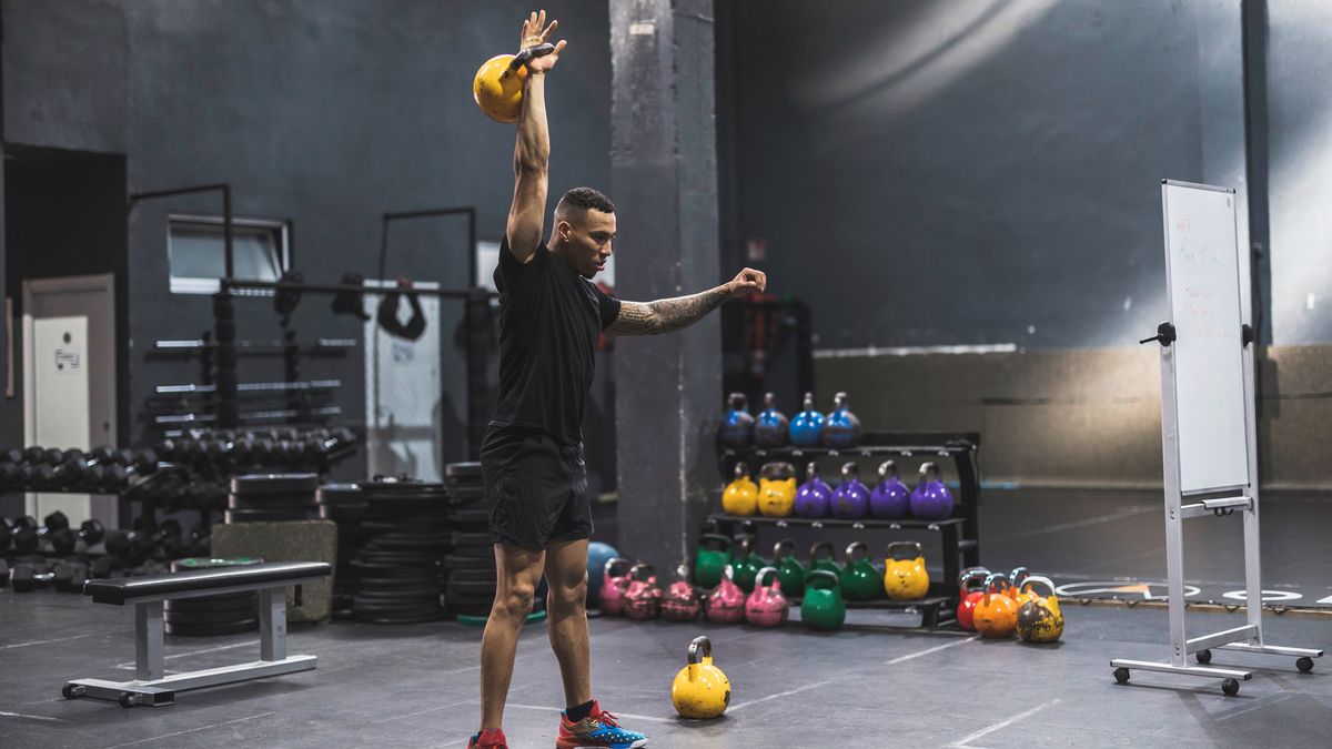 Man in gym holds kettlebell above his head