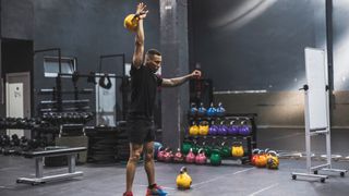 Man in gym holds kettlebell above his head