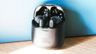 the jbl tune 225tws wireless earbuds in their charging case on a wooden surface against a blue background