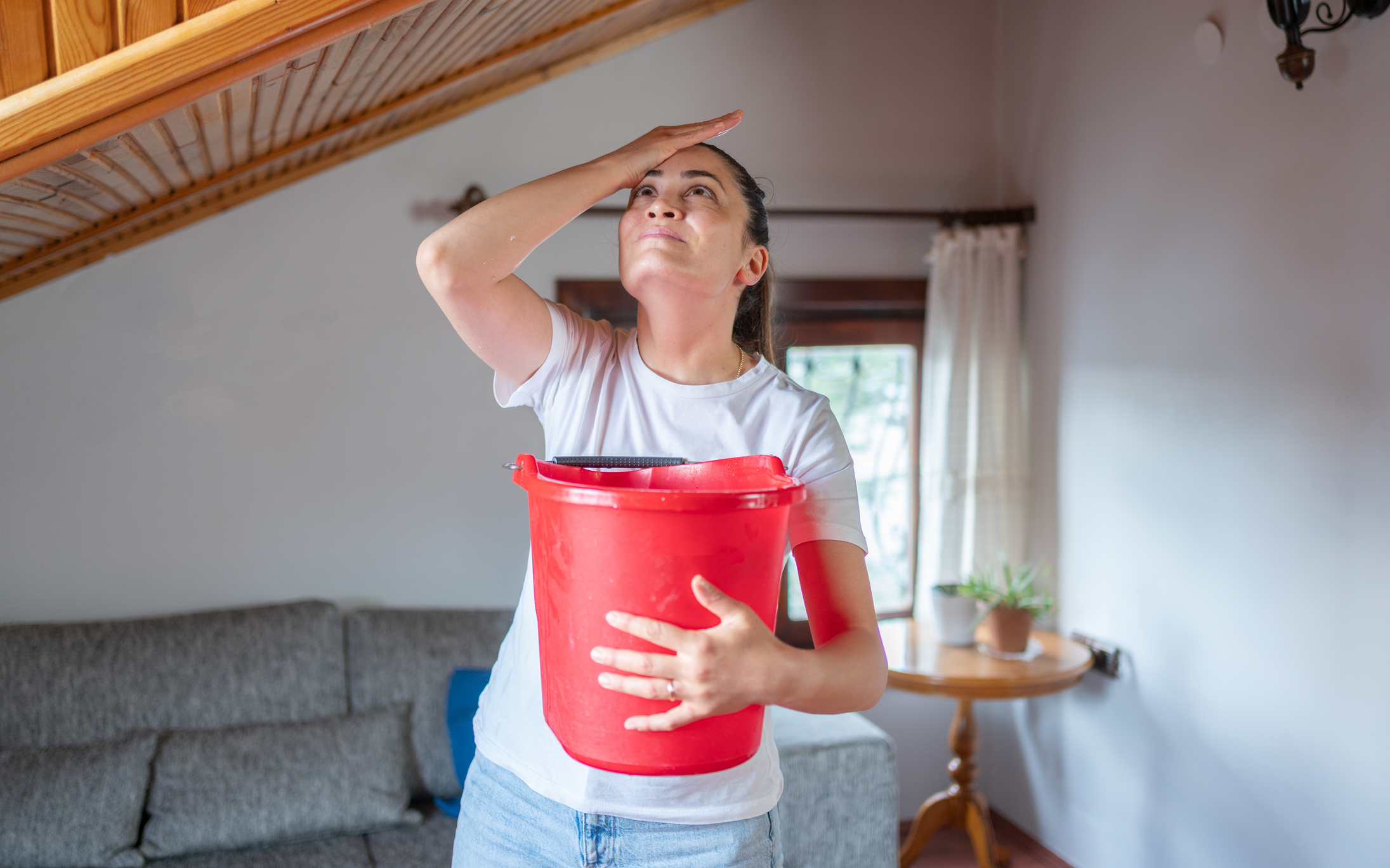a woman holding a bucket while looking at a leaky ceiling