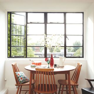 Open original 1930s Crittall window in dining area, with circular dining table and wooden chairs in front.