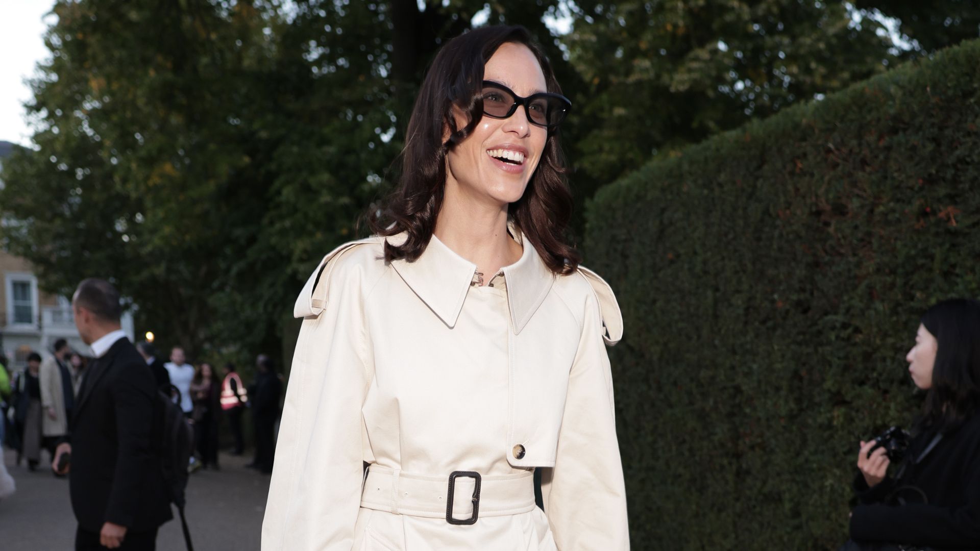 Alexa Chung wears a cream trench coat over semi-sheer tights and checked pointed-toe heels.