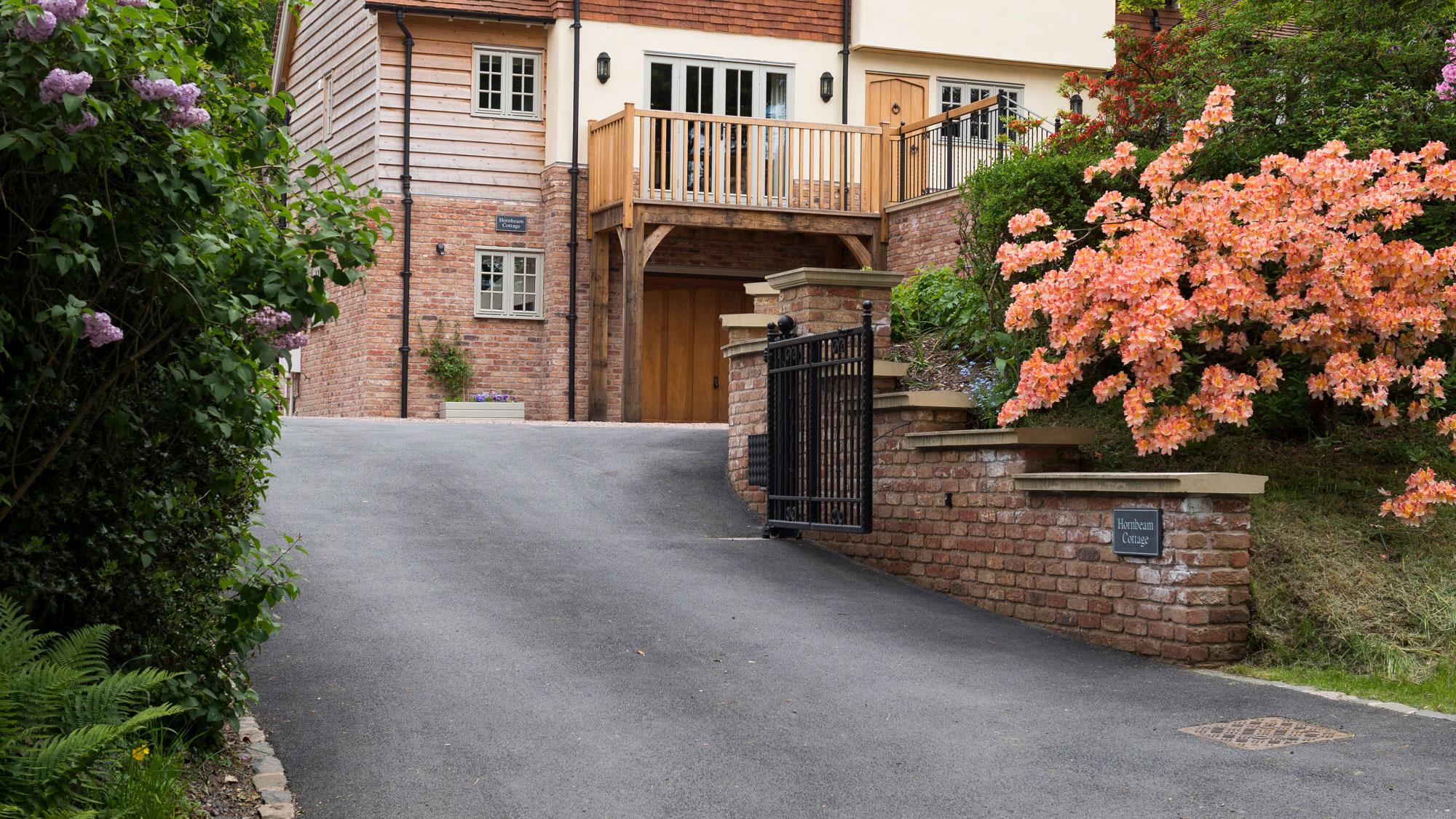 timber frame house with sloping tarmac driveway with black metal gates