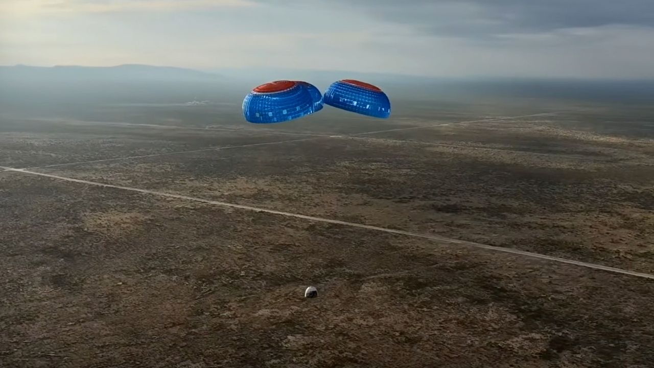A white Blue Origin space capsule lands under blue and red parachutes.