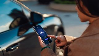 Young woman using mobile app on smartphone to manage charging electric car