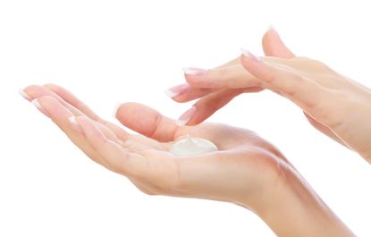 A photo of a white woman's hands; one hand is cupped and holding a blob of lotion while the other is poised to dip into the lotion