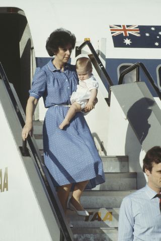 Prince William arrives in Alice Springs, Australia, during a tour with his parents, March 1983. He is carried by his nanny, Barbara Barnes