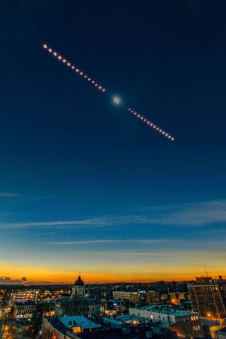 An eclipse time-lapse composite image shows the progression of a solar eclipse, framing totality in the middle in a darkening sky above a small Indiana town featuring a domed limestone courthouse at its center.