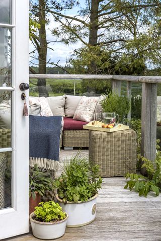 Small balcony with wicker garden furniture, throws and potted plants