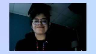 A woman with short hair sits in a dark room, taken with a NexiGo N60 webcam