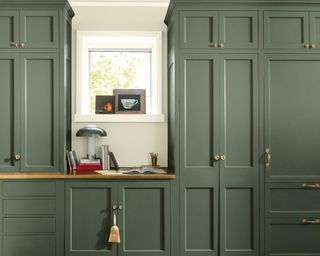 Wall to ceiling dark green cabinets with brass handles with desk area inset