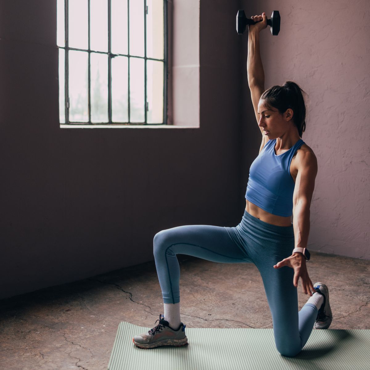 A woman doing weights in a studio, lifting a dumbbell over her head