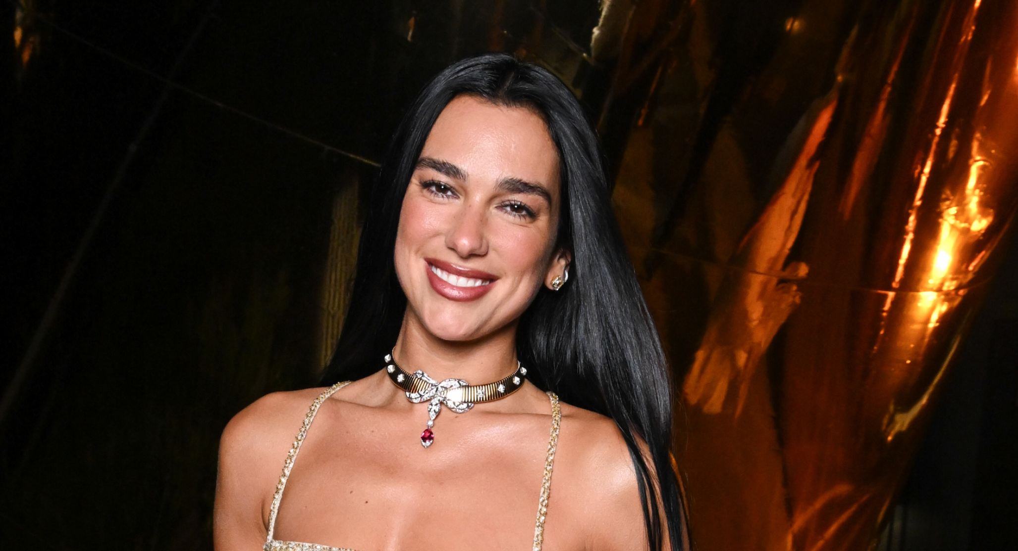 Dua Lipa wearing a gold floral vest top and smiling
