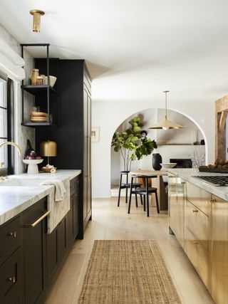 Kitchen with black cabinetry and a white marble countertop. There is a gold metallic island