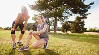 Two women sitting down on field looking at fitness trackers