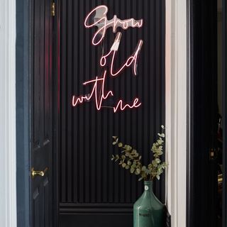 Hallway with black wall panelling with pink neon sign