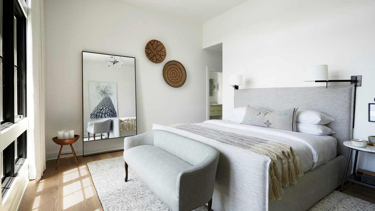 Greige minimal bedroom with large floor mirror, four poster bed and wooden round wall art pieces