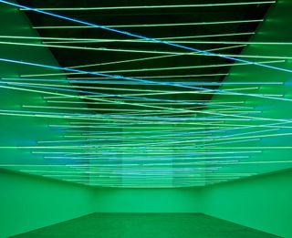 Installation view of a green, neon space with blue, yellow and green laser-style lines running horizontally across.