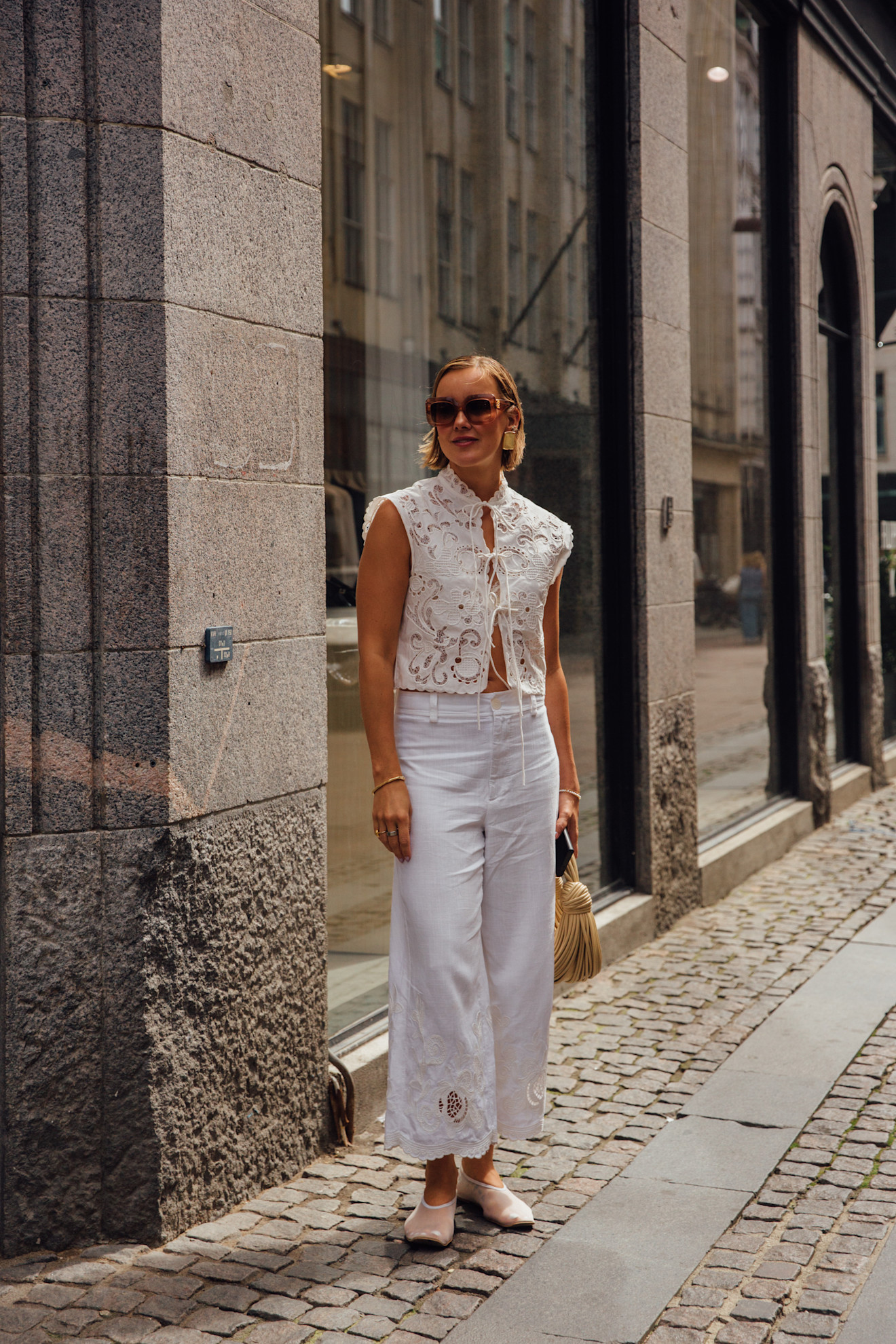a woman at Copenhagen Fashion Week weraing a white lace top, white pants, mesh flats
