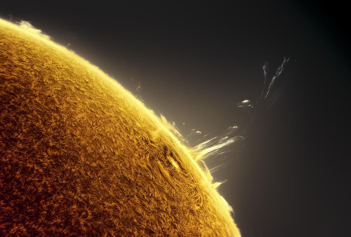 A corner of the sun sits in the bottom left of the image, as the tight loops of a solar flare jut out from just over the solar horizon.