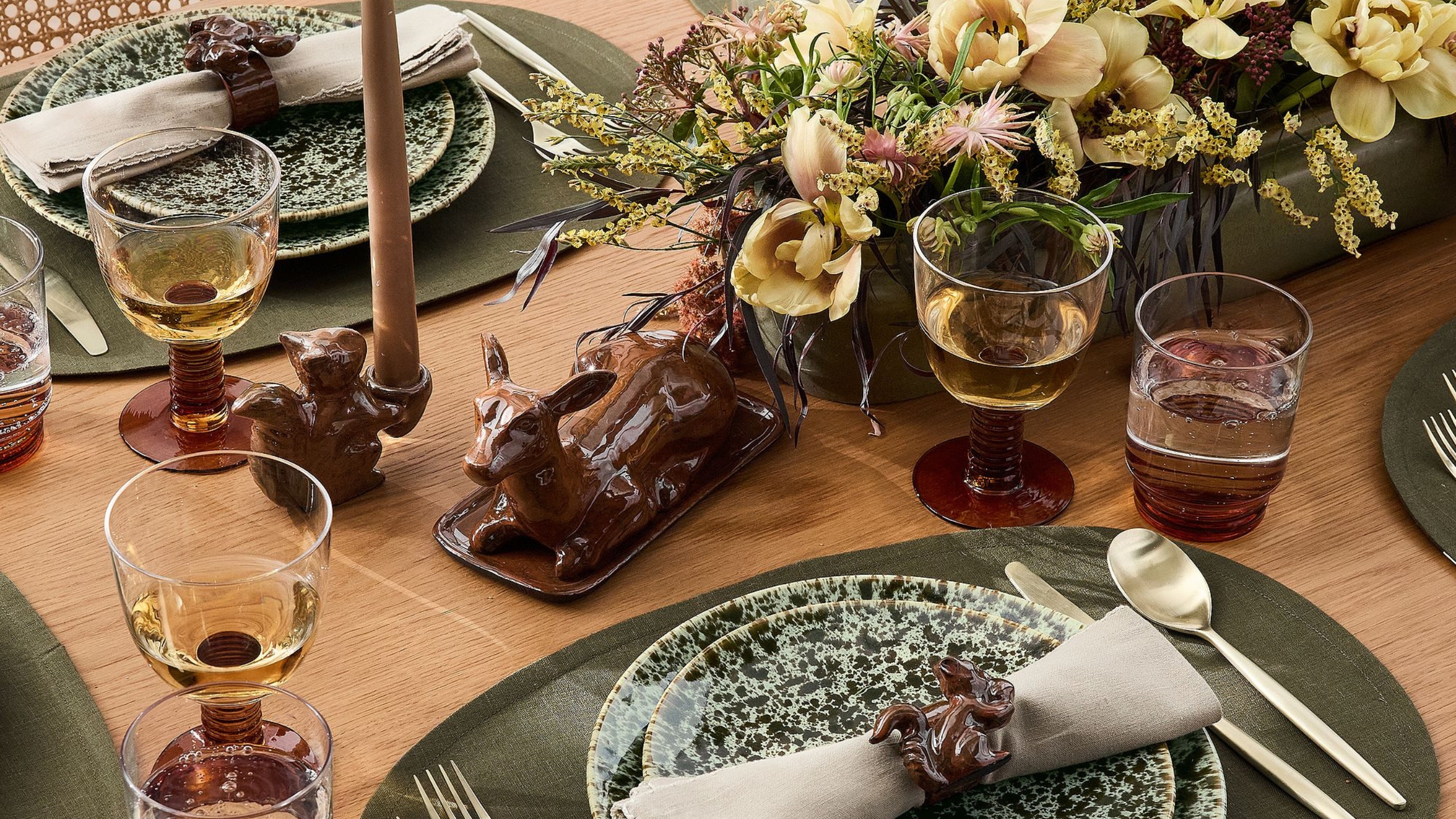 A tablescape of speckled plates, florals, candles and a beautiful deer shaped butter dish 