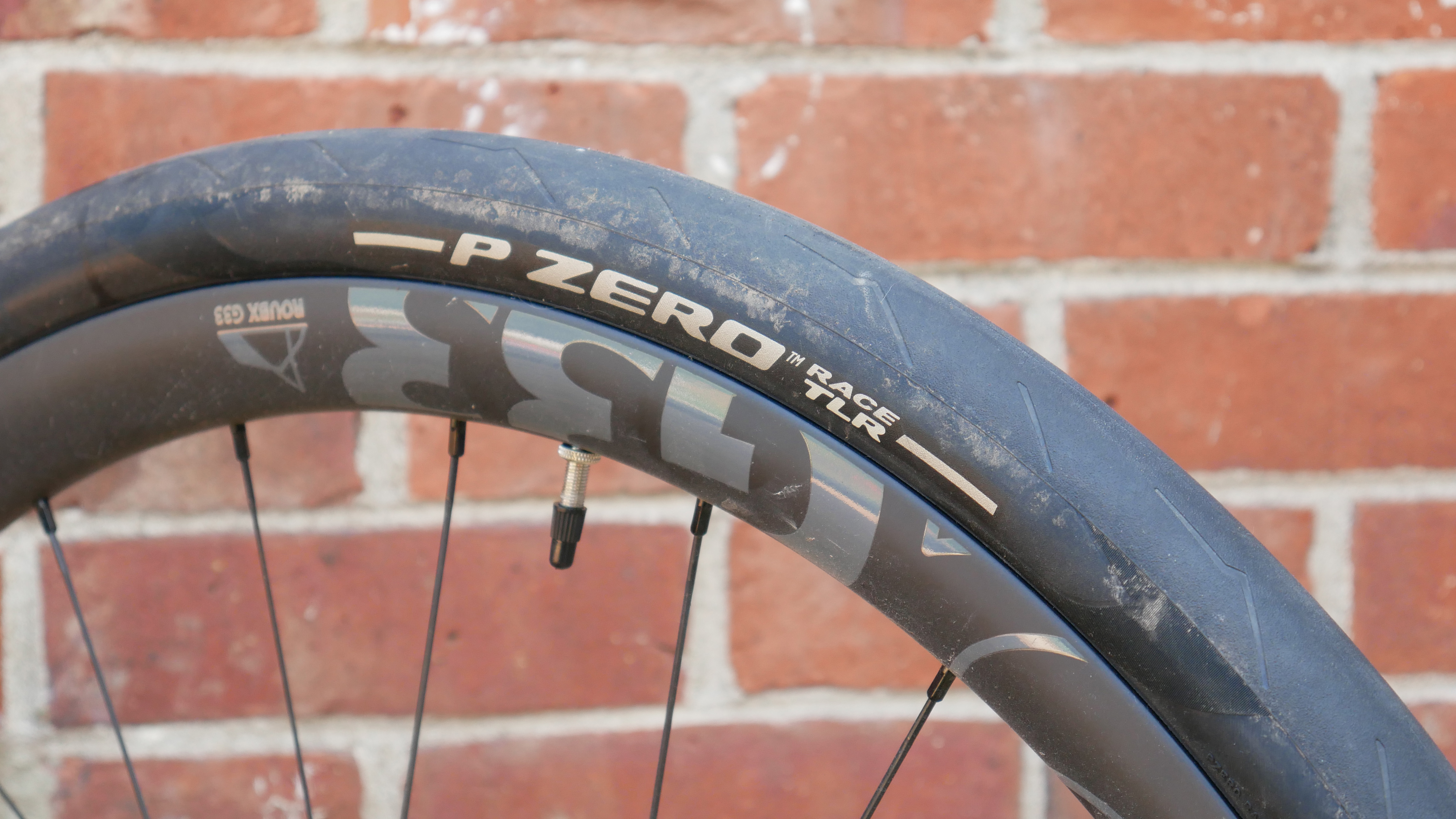 A black Pirelli P-Zero Race TLR tyre with white writing mounted to a Token wheel in front of a red brick wall