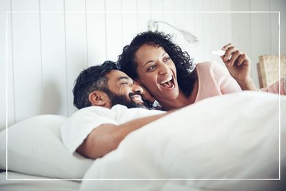 Couple in bed and smiling at a positive pregnancy test