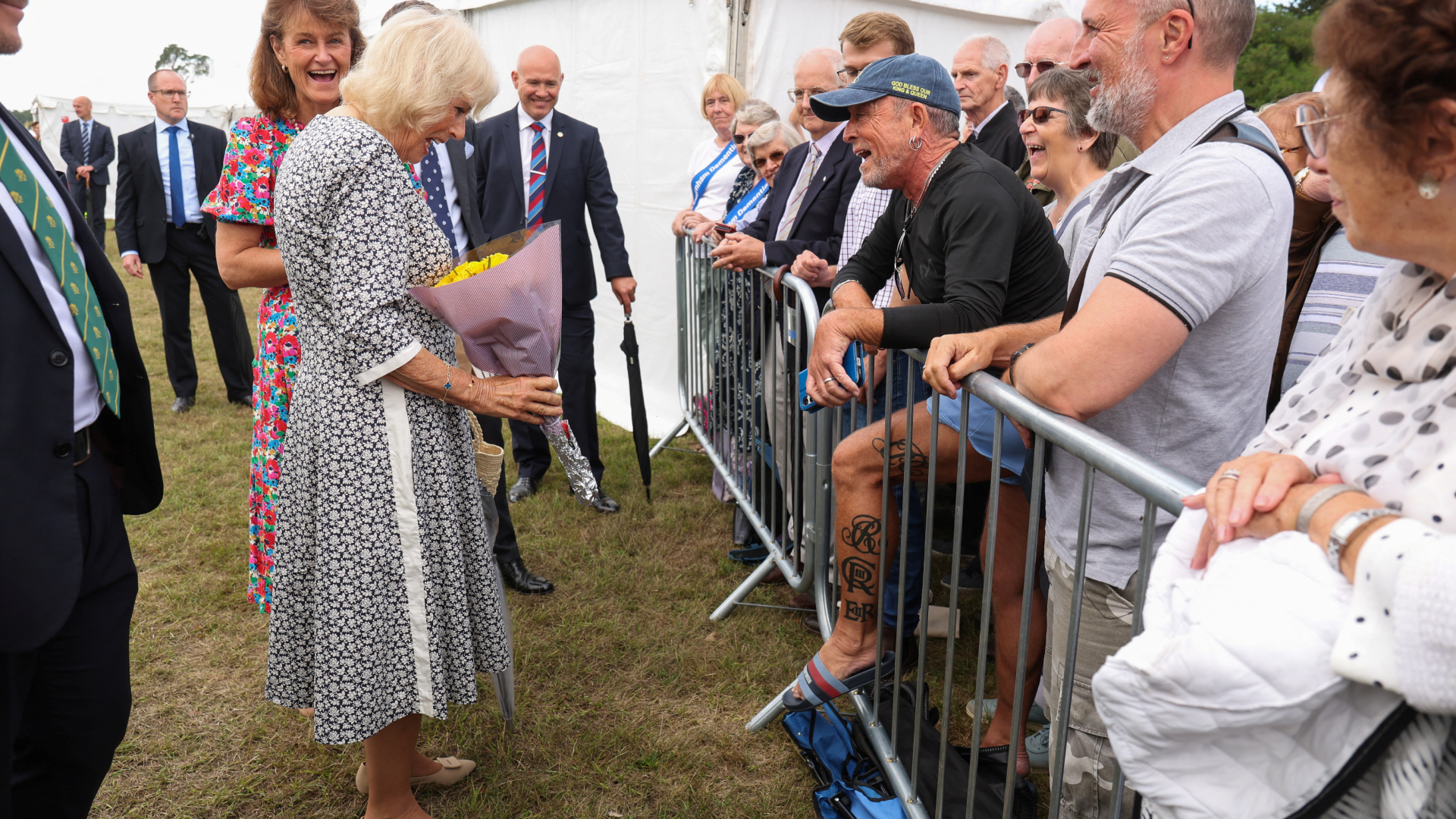 Queen Camilla looking at a man's tattoos in a crowd with a shocked expression