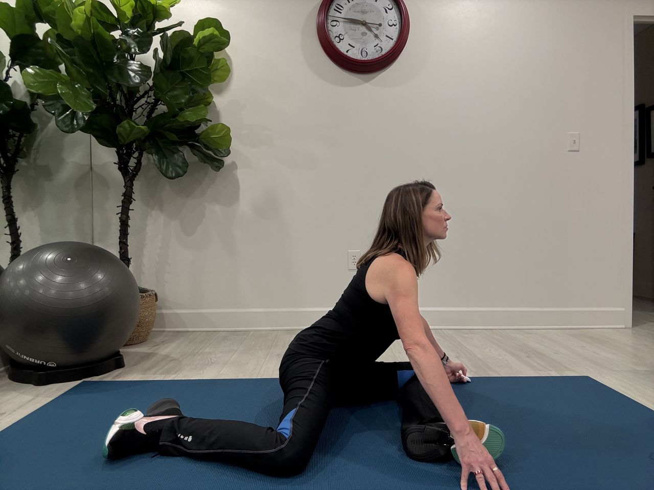 An employe at Femina physical therapy performs 90/90, sitting on the floor, hands in front, left leg in front and right leg to the side, both bent to 90&deg;.