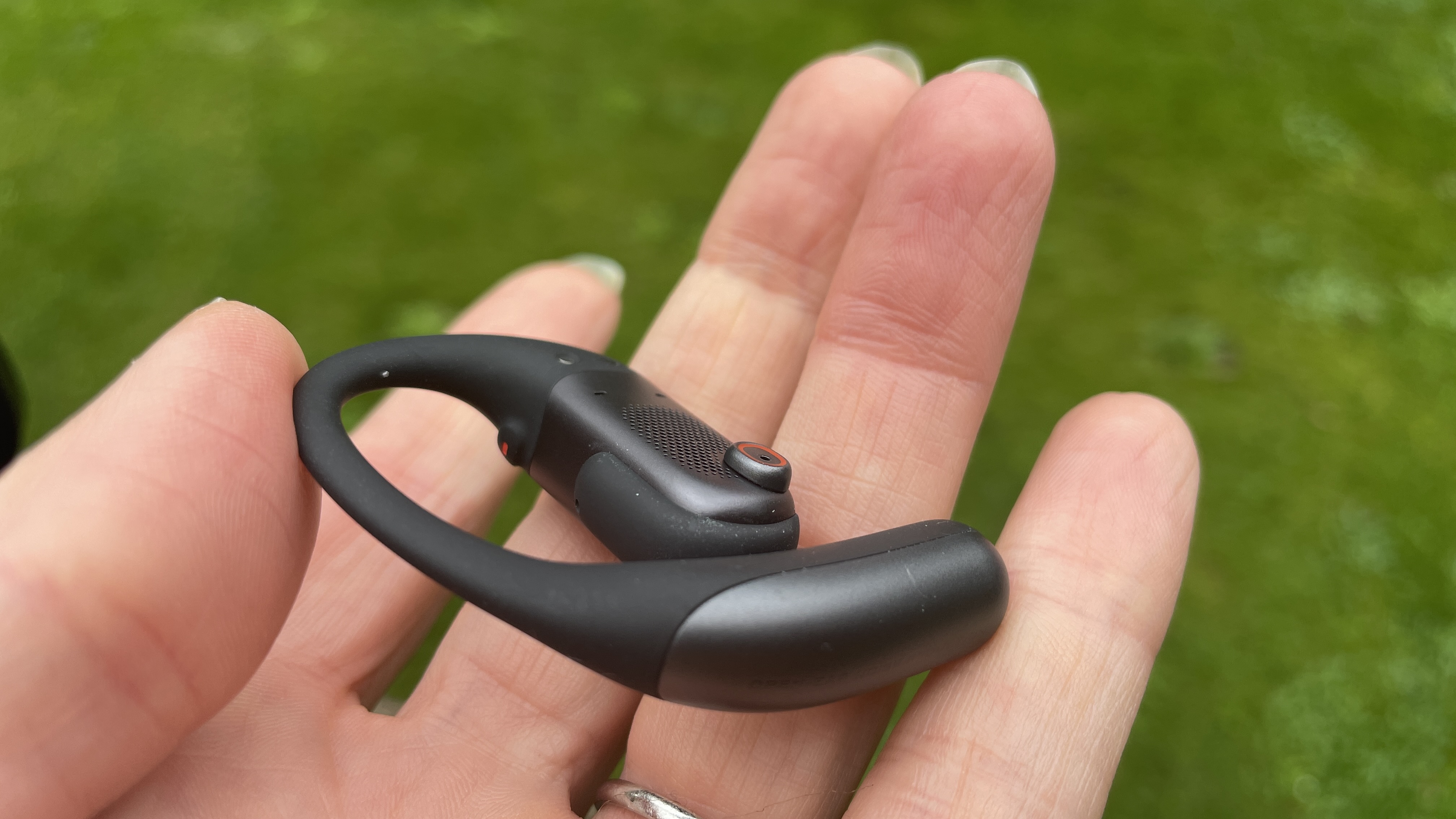 Shokz Openfit Pro outside, outside held in a woman's hand, with green grass in the background