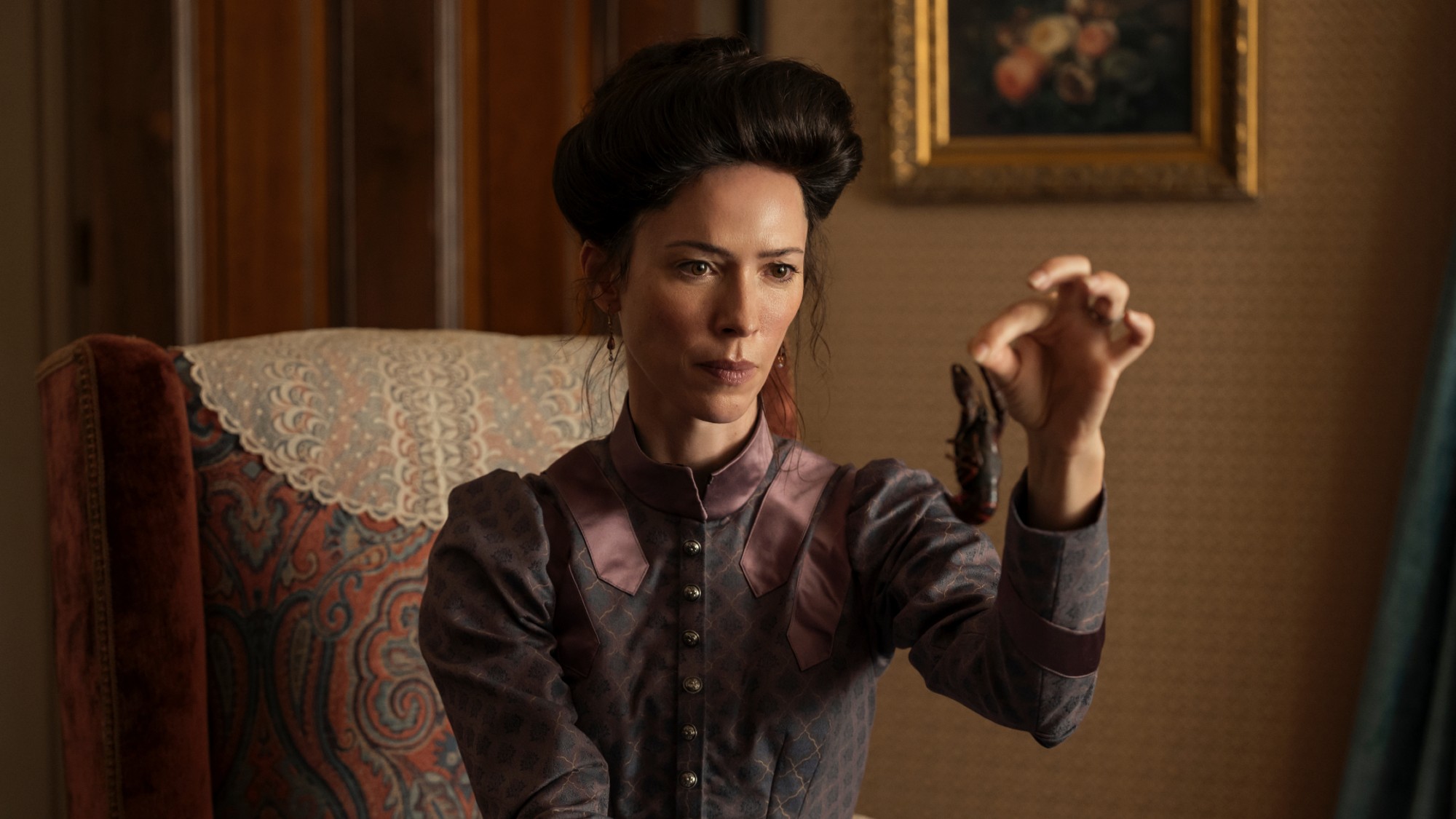 Mrs. Borden examines a crawfish that was served as part of their dinner. She has a disapproving look on her face and is wearing a green victorian-era dress.