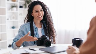 Joyful Professional Photographer Lady Holding Camera Using Laptop At Workplace
