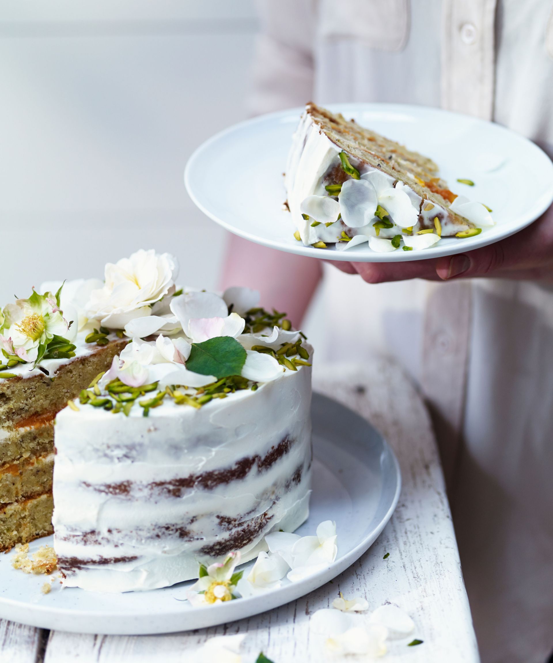 multi-layered rose and apricot cake with crumb coating, white flower petals and pistachios on top