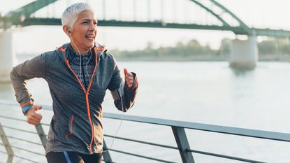 A woman wearing earbuds jogs over a bridge.