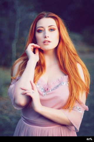 A portrait image of a redheaded woman in a pink dress, standing in a woodland, taken with the Olympus Vintage I Art FIlter