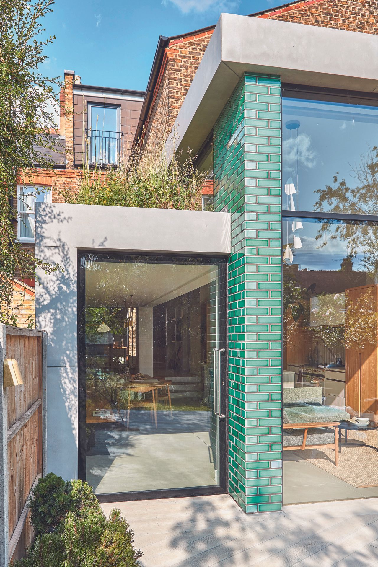 The blue tiled back exterior of the house with a large glass wall and door leading to the garden