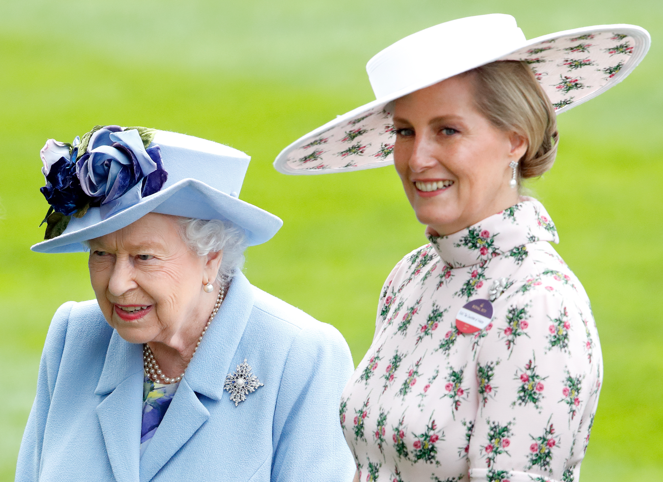 Queen Elizabeth wearing a blue hat and coat and Duchess Sophie in a pink floral dress and hat at Royal Ascot