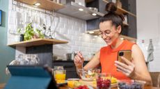 Woman sitting at table eating foods to help relieve constipation quickly, holding phone in hand and smiling