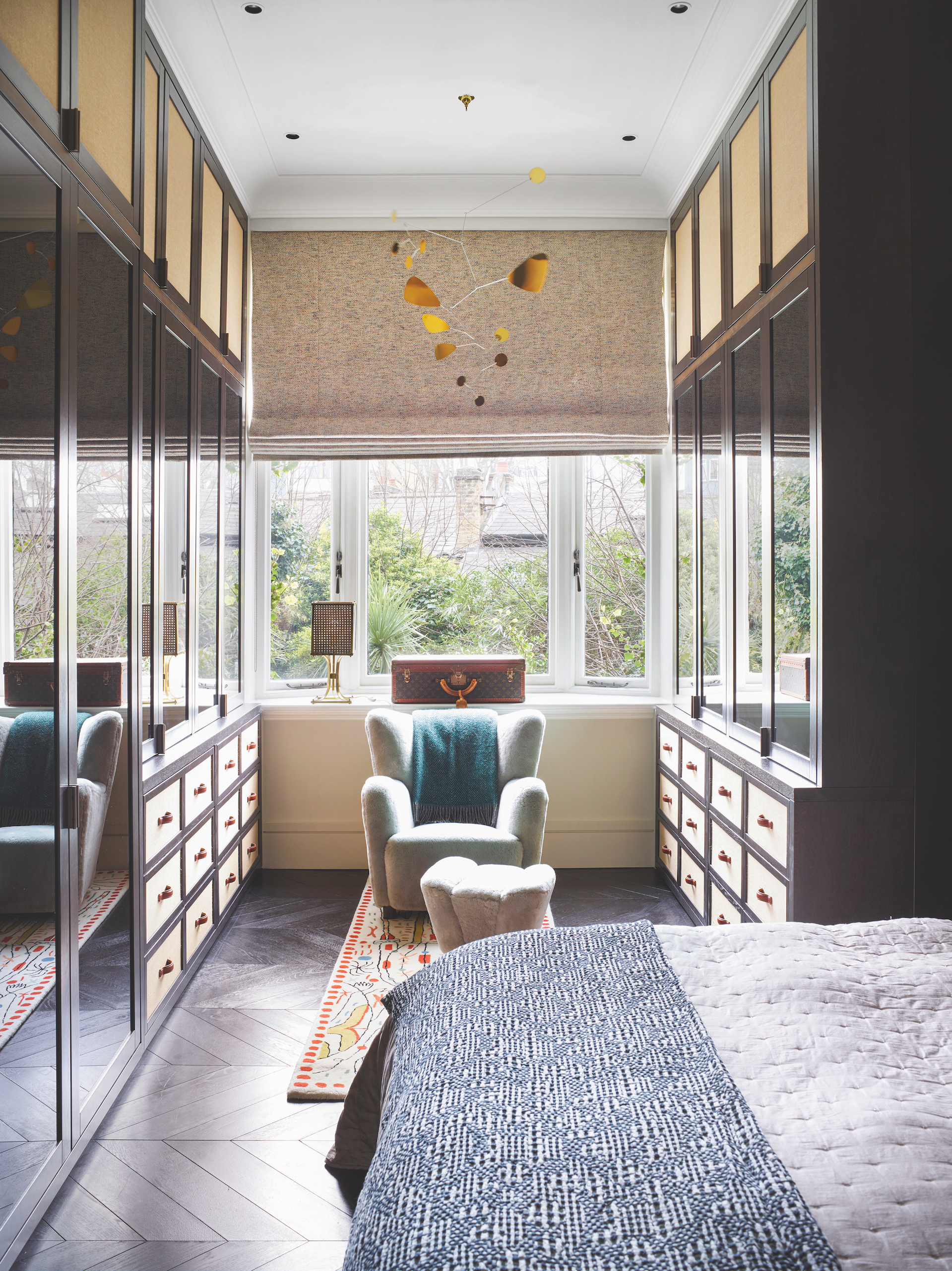 Bedroom with bed, armchair and footstool, custom clothes storage, and chevron parquet floor