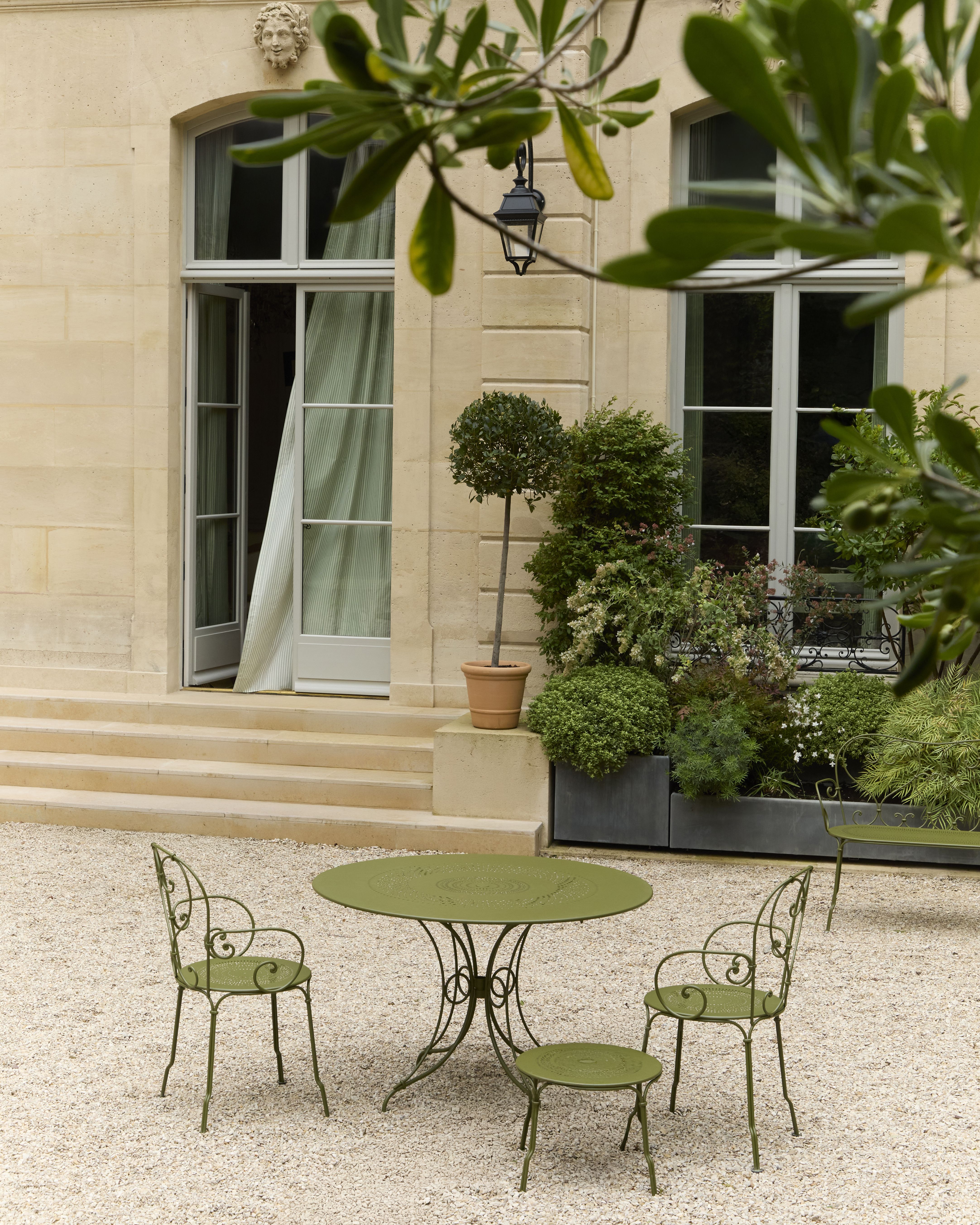 A picturesque courtyard decorated with lush vegetation and green-painted art nouveau iron furniture.