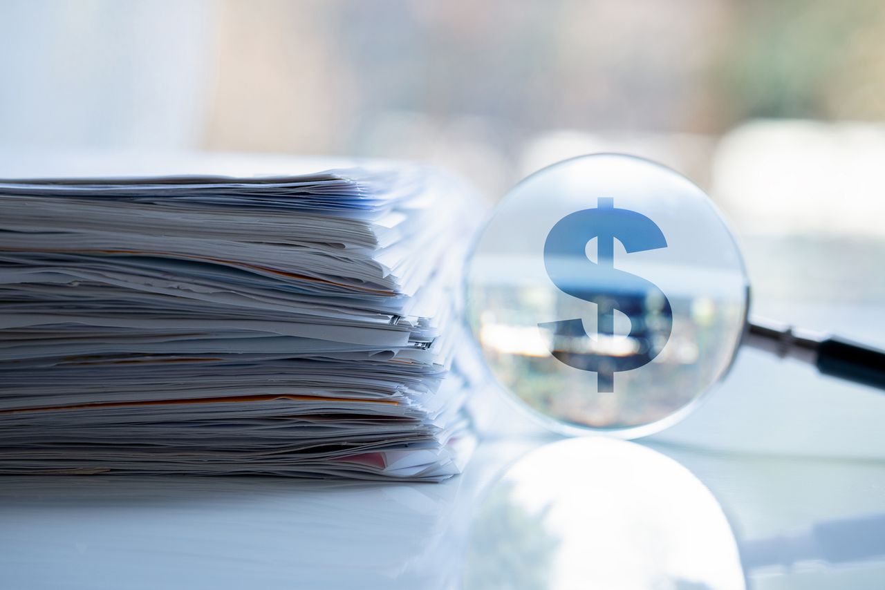 image of files on a table next to a magnifying glass over a dollar sign